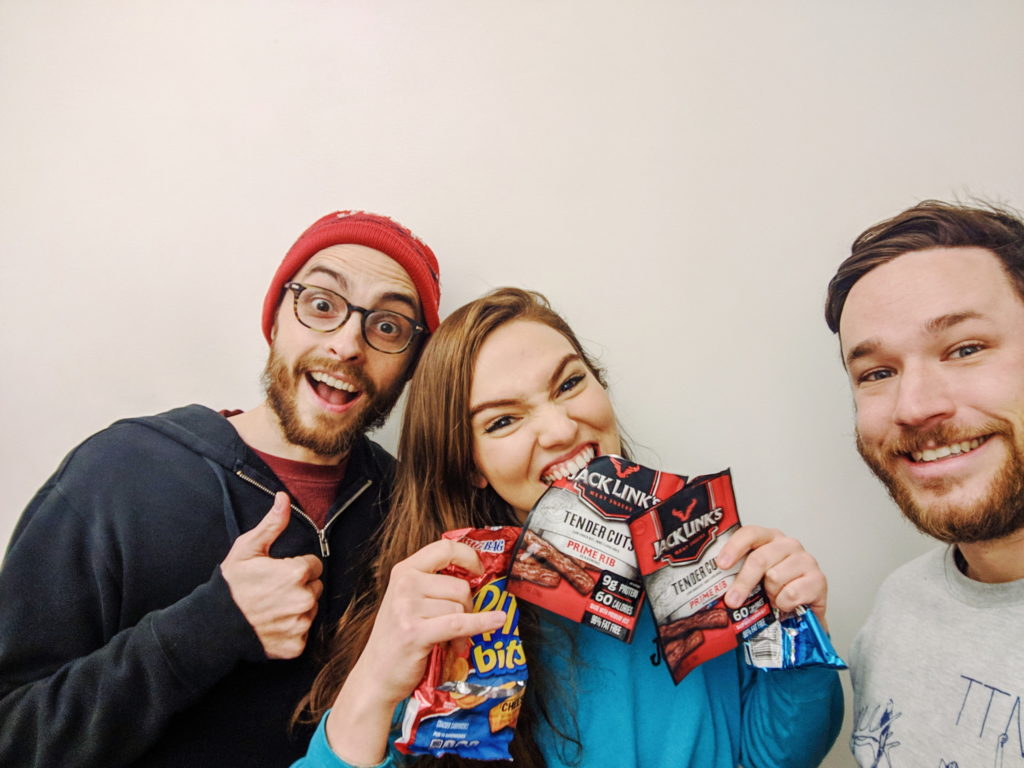 Evan Forde Barden, Addie Weyrich, and Patrick Cartelli taking a selfie. Addie is holding packs of beef jerky.